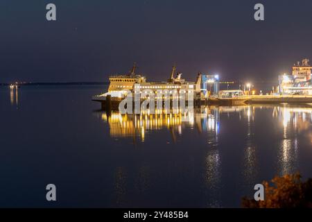 Un ferry se trouve dans un port animé la nuit, éclairé par des lumières vibrantes. L'eau calme crée un reflet époustouflant, offrant une atmosphère paisible Banque D'Images