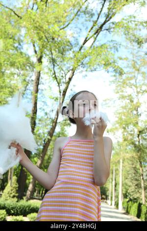 Portrait de petite fille mangeant de la barbe à papa sucrée dans le parc, vue d'angle bas Banque D'Images