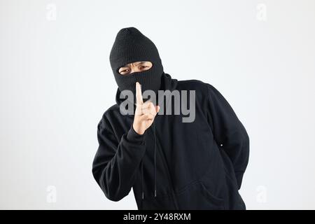 Voleur en Balaclava noir tenant les doigts sur les lèvres, faisant Hush Sign, isolé sur fond blanc Banque D'Images