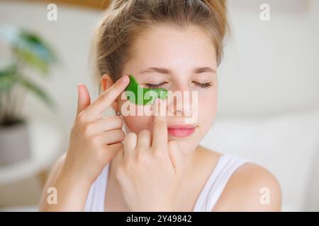 Une jeune femme appliquant un patch vert sous les yeux pour réduire les poches et les cernes. Banque D'Images