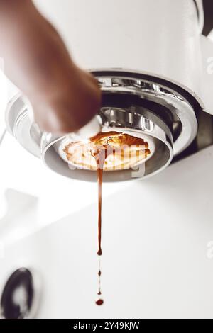 Gros plan d'un délicieux flux d'espresso à partir d'un porte-filtre sans fond, créant un crémite riche sur fond lumineux Banque D'Images