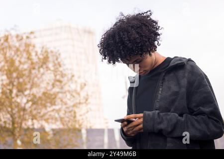 adolescent avec des cheveux bouclés à l'aide d'un téléphone portable Banque D'Images
