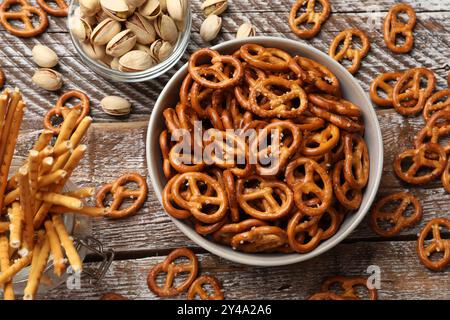 Délicieux craquelins de bretzel, bâtonnets salés et pistaches sur table en bois, pose à plat Banque D'Images