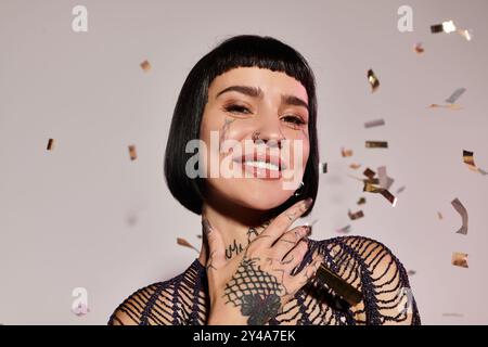 Une femme tatouée sourit brillamment tout en étant entourée de confettis festifs. Banque D'Images