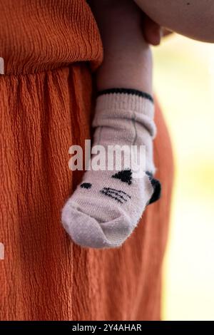 Un gros plan portrait de la jambe et du pied mignons d'un bébé portant une chaussette confortable pressée en toute sécurité contre la mère attentionnée qui s'occupe du petit enfant. Banque D'Images