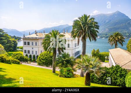 Nichée par les eaux tranquilles du lac de Côme, la Villa Melzi présente une architecture néoclassique au milieu de jardins luxuriants et de montagnes majestueuses sous un ciel bleu vif. Banque D'Images