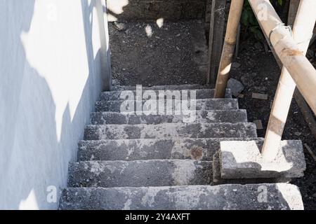 Un ensemble d'escaliers en béton menant vers le bas, partiellement recouverts de poussière et de saleté. Les escaliers sont flanqués d'une balustrade en bambou d'un côté, et le surrou Banque D'Images