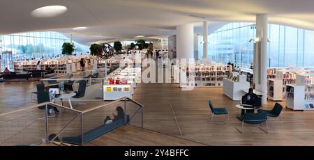 Helsinki, Finlande, le 18 juillet 2024 : L'intérieur moderne de la bibliothèque est baigné de lumière naturelle et les gens naviguent ou lisent par un après-midi calme. Bibliothèque Oodi Banque D'Images