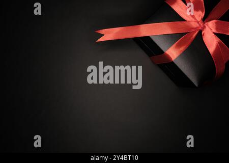 Boîte cadeau noire enveloppée avec ruban de satin en forme d'arc, sur fond noir. La boîte est située dans le coin supérieur droit de l'image, partie Banque D'Images