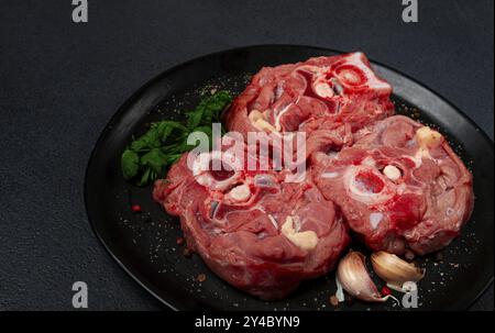 Steak cru, cou de veau sur l'os, viande fraîche, sur une assiette noire, vue de dessus, personne Banque D'Images