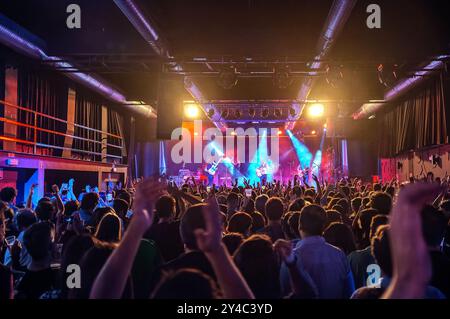 Concert rock dynamique en salle avec un public animé et des musiciens se produisant sur une scène bien éclairée, créant une atmosphère énergique remplie de mu Banque D'Images