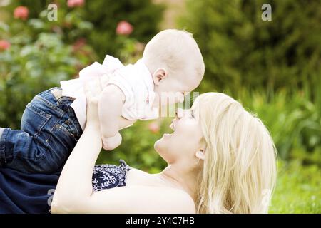 Heureuse jeune femme jouant avec bébé garçon dans le jardin fleuri de printemps. Arrière-plan flou de nature Banque D'Images