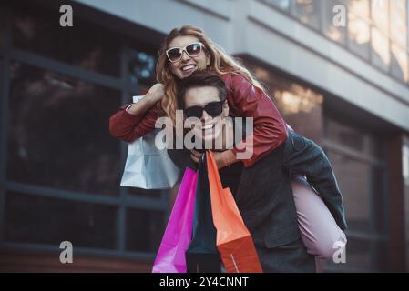 Heureux couple magasinant ensemble et s'amusant. Petit ami portant sa petite amie sur le piggyback Banque D'Images