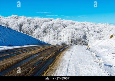 La route qui longe le sommet de la montagne est couverte de neige humide et sale. Banque D'Images