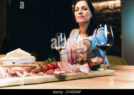 Main femelle prenant une amande d'un plat en bois avec prosciutto, fromage, pruneaux, noix et tomates cerises servi en accompagnement, gros plan. Banque D'Images