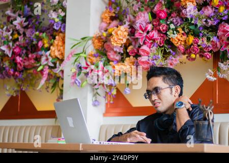 bel homme d'affaires asiatique masculin dans la douleur à l'épaule devant l'ordinateur portable sur la table, assis dans le lieu de travail de café. pour la santé, l'éducation, technolo Banque D'Images
