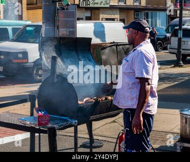 Suffern, NY - US - Sep 15, 2024 Un vendeur grille de la viande sur un grand fumeur en plein air à la foire de Suffern Street, avec de la fumée qui monte dans l'air. Le jour attra Banque D'Images