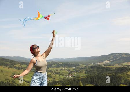 Femme souriante volant cerf-volant dans les montagnes sous le ciel bleu. Espace pour le texte Banque D'Images