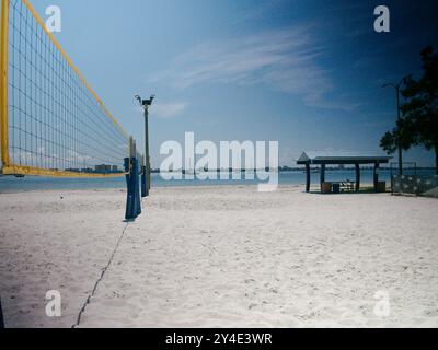 Vue large avec filet de volley-ball à bord jaune sur la gauche avec une vue sur une plage de sable blanc lors d'une journée ensoleillée en Floride. Pavillon couvert Banque D'Images