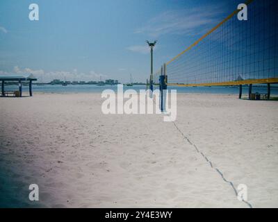 Vue large avec filet de volley-ball à bord jaune sur la droite avec une vue sur une plage de sable blanc lors d'une journée ensoleillée en Floride. Voiliers en baie Banque D'Images