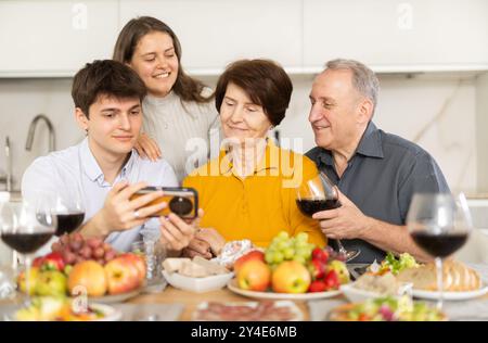 Les parents heureux et leurs enfants regardent et discutent des photos d'eux ensemble sur l'écran du smartphone Banque D'Images