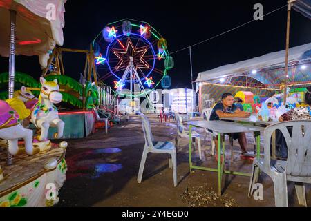 Grande roue incandescente en arrière-plan. Au parc d'attractions local, pauvre, au bord de la rivière du Mékong la nuit à Vientiane, Laos. Banque D'Images