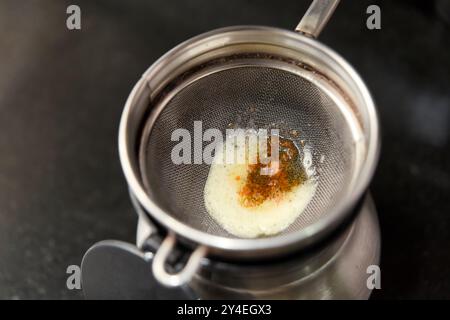 Du ghee fraîchement préparé filtré à travers un tamis métallique, séparant la bonté dorée pour les délices culinaires. Banque D'Images