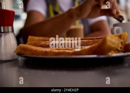 Femme garder des tartes de churros dans la main entendue. Churros populaire délicieux plat espagnol avec chocolat chaud, sucre et café sur la table du restaurant avec blured b Banque D'Images