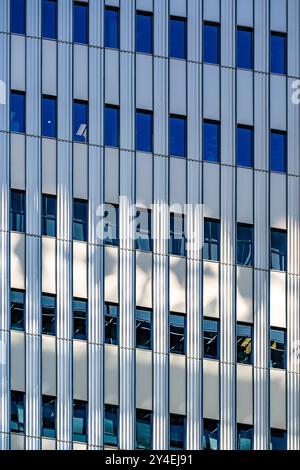 Bâtiment contemporain de plusieurs étages en métal et verre avec des formes géométriques strictes et des rebords et un motif répétitif de fenêtres se précipite dans le s. Banque D'Images