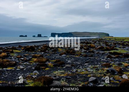 Plage de galets de lave noirs avec des vagues s'écrasant clément sur les falaises de roche de lave noire avec de belles piles à Reynisdrangar à Vik en Islande Banque D'Images