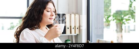 La belle femme plus grande taille savoure sa boisson, enveloppée dans la tranquillité matinale au bureau. Banque D'Images