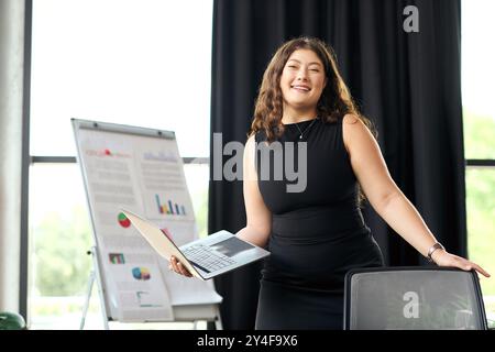 Une femme de taille plus confiante avec de longs cheveux bouclés collabore activement dans un cadre de bureau lumineux, mettant en valeur son professionnalisme. Banque D'Images