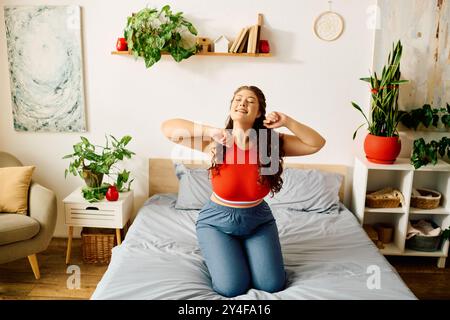 Une jeune femme de grande taille sourit alors qu'elle s'étire de manière ludique sur son lit, entourée de belles plantes et de soleil. Banque D'Images