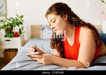 Une jeune femme de grande taille avec de beaux cheveux bouclés se détend sur son lit, notant des pensées dans un cahier à la maison. Banque D'Images