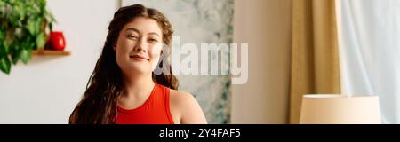 Une jeune femme belle grande taille aux cheveux bouclés profite d'un moment de détente à la maison, rayonnant de chaleur et de confiance. Banque D'Images