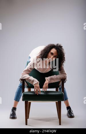 Une jeune femme aux cheveux bouclés se penche sur une chaise dans un studio, les bras tendus et les mains reposant sur le siège Banque D'Images