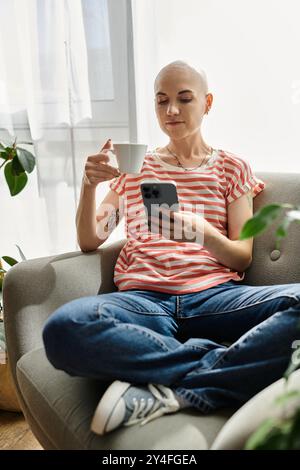 Une jeune femme atteinte d'alopécie sirote du café et vérifie son téléphone dans un espace confortable et lumineux. Banque D'Images