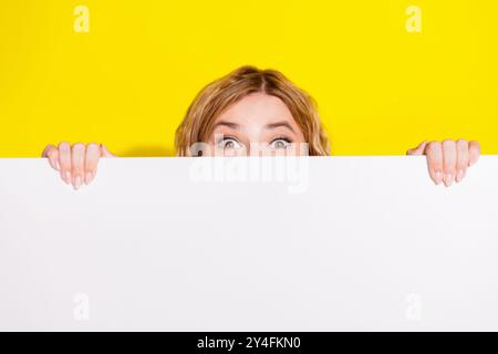 Photo d'adorable belle fille se levant se cachant derrière l'écriteau blanc espace vide isolé fond de couleur jaune Banque D'Images