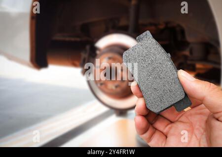 Concept de maintenance du système de freinage de voiture , main mécanique tenant une plaquette de frein de voiture avec système de freinage d'une automobile sans roue sur fond Banque D'Images