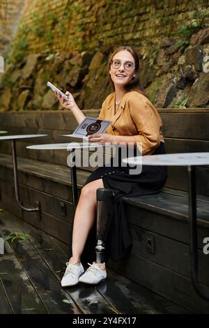 Dans un charmant café, une jeune femme avec une jambe prothétique s'engage avec son téléphone, rayonnant de joie et de confiance. Banque D'Images