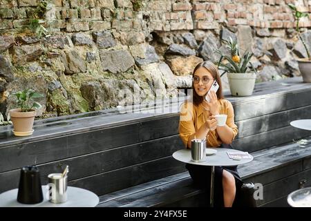 Une jeune femme est assise confortablement dans un café confortable, sirotant sa boisson et embrassant son voyage unique avec confiance. Banque D'Images