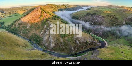 Une fine couche de brume roule à travers la vallée tandis que le soleil du matin illumine la colline. Dovedale Peak District Derbyshire Royaume-Uni Banque D'Images