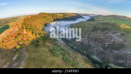 Une fine couche de brume roule à travers la vallée tandis que le soleil du matin illumine la colline. Dovedale Peak District Derbyshire Royaume-Uni Banque D'Images