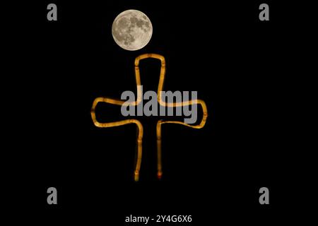 Aqosh, Irak. 17 septembre 2024. La pleine lune se lève derrière une croix placée au sommet d'un bâtiment dans la ville irakienne d'Alqosh, à 50 km au nord de Mossoul. Crédit : SOPA images Limited/Alamy Live News Banque D'Images