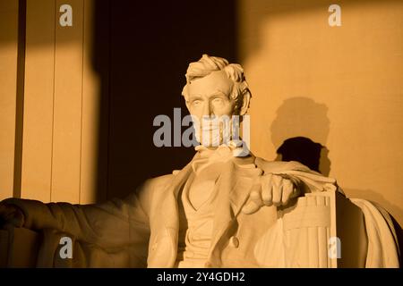 Statue du Lincoln Memorial Mur d'ombre Washington DC | WASHINGTON D.C., États-Unis — Le buste et la main droite puissante d'Abraham Lincoln par Daniel Chester French au Lincoln Memorial, éclairé par le soleil matinal de l'équinoxe, avec l'ombre de Lincoln projetée avec netteté sur le mur arrière de la salle. French a délibérément dimensionné la figure assise à 19 pieds (5,8 m) — des études ont montré que si Lincoln se tenait debout, il atteindrait 28 pieds (8,5 m) — afin que la statue ne soit pas éclipsée par l'intérieur de 60 pieds (18,3 m) du mémorial. Note : la couleur et l'éclairage sont entièrement naturels, aucun filtre n'a été appliqué. Banque D'Images