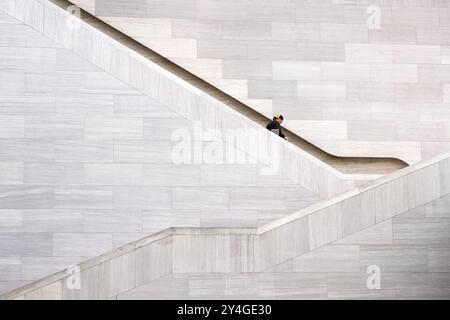 National Gallery of Art Staircase Washington DC | WASHINGTON D.C., États-Unis — Un visiteur descend un escalier en pierre à l’intérieur du bâtiment est de la National Gallery of Art, conçu par l’architecte I.M. Pei. Ouvert en 1978, le bâtiment associe des murs en béton angulaires à des escaliers fortement inclinés qui transforment la circulation simple en une étude de géométrie, de lumière et d’ombre. Banque D'Images