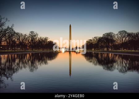 WASHINGTON DC, États-Unis — le Washington Monument, le dôme du Capitole des États-Unis et la piscine réfléchissante vus depuis le Lincoln Memorial au lever du soleil pendant l'équinoxe de printemps et d'automne. Le soleil se lève parfaitement aligné avec le National Mall, projetant une lueur chaude sur les monuments emblématiques. Banque D'Images