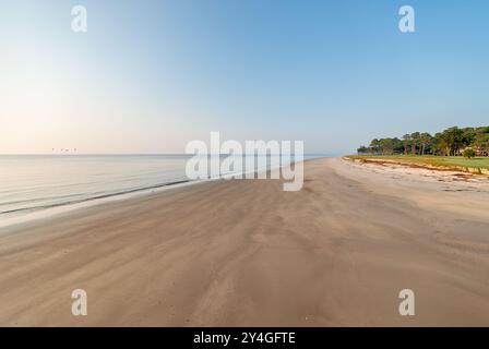 ÎLE DE DAUFUSKIE, Caroline du Sud, États-Unis — Une plage immaculée s'étend devant un complexe hôtelier sur l'île de Daufuskie, mettant en valeur la beauté naturelle intacte de cette destination isolée du Lowcountry. Le vaste littoral sablonneux rencontre les eaux de l'océan Atlantique, offrant aux visiteurs une retraite côtière tranquille. Banque D'Images