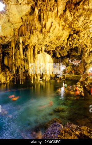 Cenote Xkakah Stalactites souterraines Nageurs Yucatan Mexique | VALLADOLID, Yucatan, Mexique — Des nageurs portant des gilets de sauvetage flottent sous une formation massive de stalactites à l'intérieur du Cenote X'kakah (également connu sous le nom de Cenote Dzitnup), une doline semi-souterraine à l'ouest de Valladolid. Les quelque 6 000 cenotes connues de la péninsule du Yucatan se sont formées lorsque l'eau de pluie a dissous le socle calcaire poreux de la région, provoquant finalement l'effondrement du plafond et l'exposition de la nappe phréatique — le même aquifère dont les anciens Mayas dépendaient entièrement, car la péninsule ne compte aucune rivière de surface. Banque D'Images