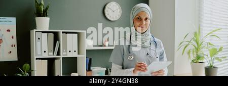 Médecin féminin souriant dans le bureau moderne tenant la tablette Banque D'Images
